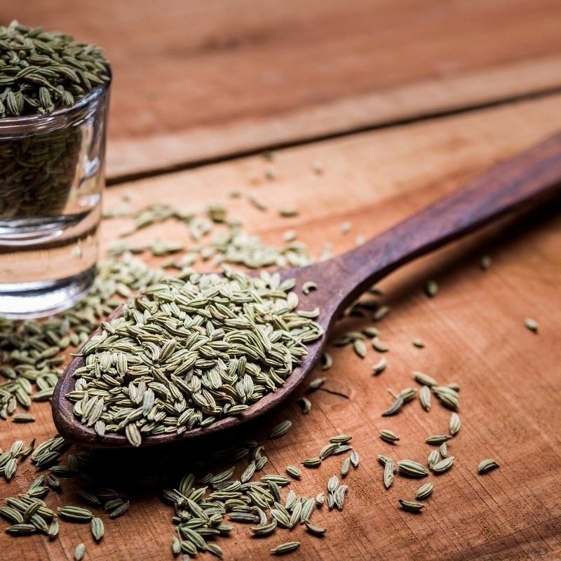 fennel seeds in a wooden spoon and in a glass fennel seeds in a wooden spoon and in a glass