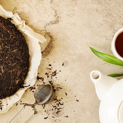 red tea on a paper next to an infuser, a teapot and a cup of tea