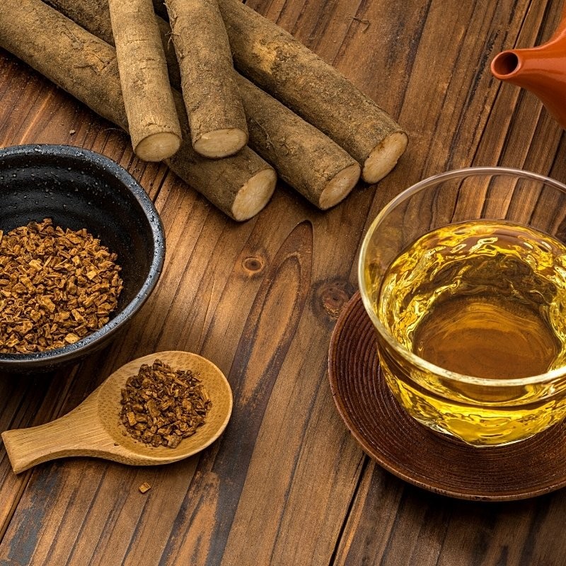 whole and fragmented burdock roots on the table and next to a tea