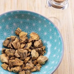 dried gentian roots in a bowl next to a glass jar