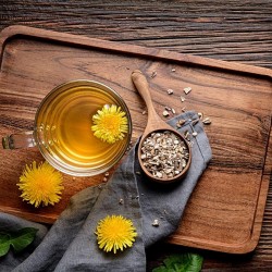 Fragmented dandelion root in a wooden spoon next to a tea and fresh flowers and leaves