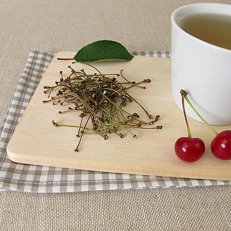 pés de cereja sobre uma tabua de cozinha, junto a uma chávena de chá e às bagas e uma folha de cerejeira