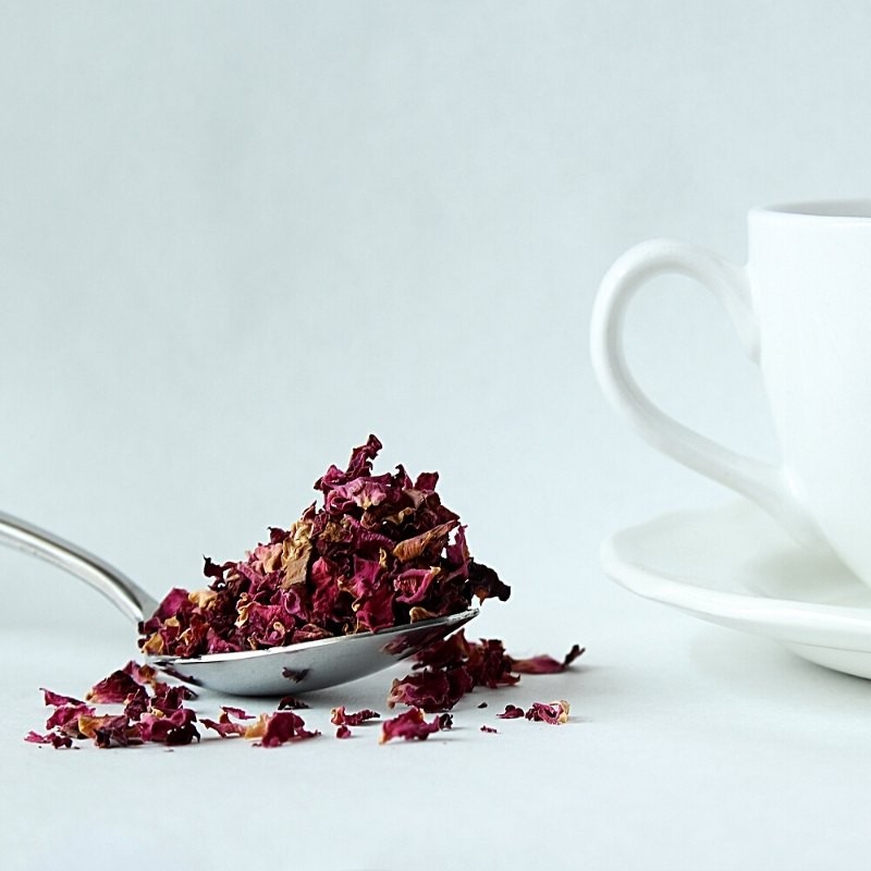 French rose petals on a spoon next to a cup French rose petals on a spoon next to a cup